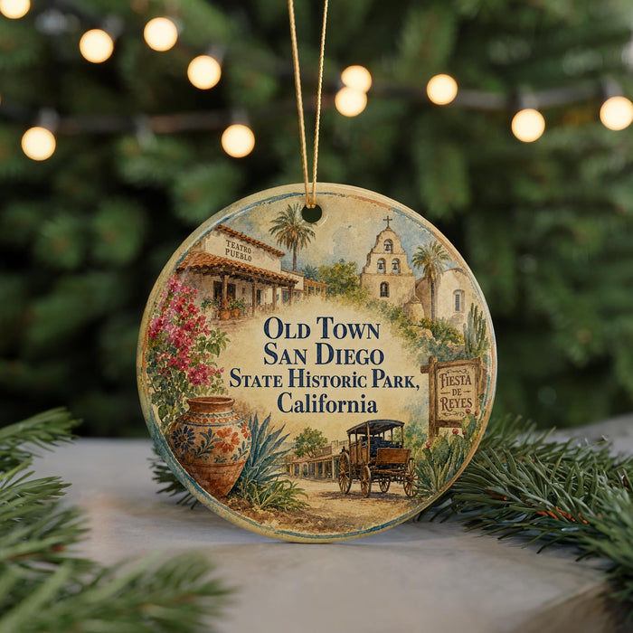 A round ornament featuring a painting of Old Town San Diego, California, with a Santa Claus and reed sign, surrounded by greenery and a string of lights.