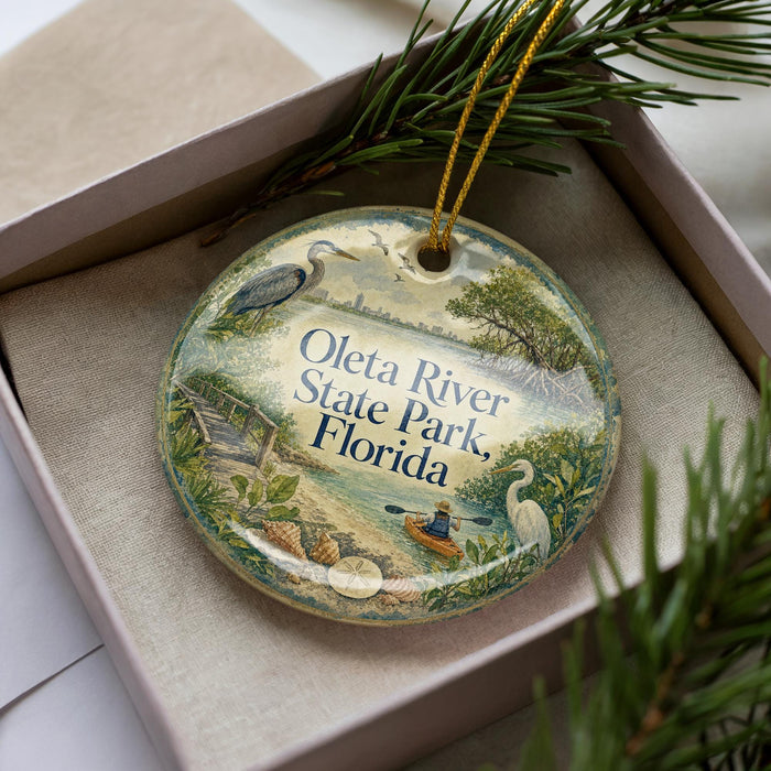 A decorative ornament in a box, featuring illustrations of a river, park, and wildlife, with the text "Oleta River State Park, Florida" prominently displayed.