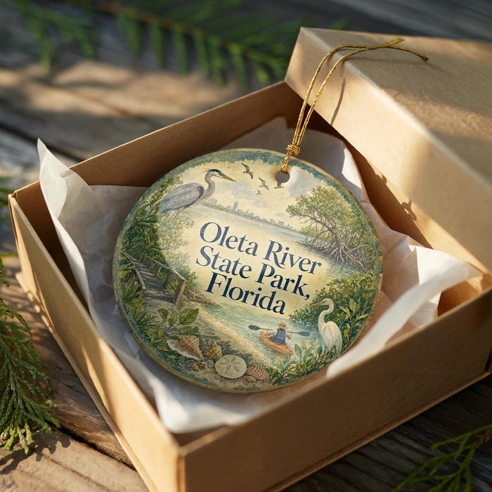 A circular ornament with a bird and a boat, placed in a cardboard box with a gold string.