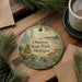 A round ornament with a scenic image of Onaway State Park, Michigan, is displayed on a wooden surface alongside a cup of coffee and some pine branches.