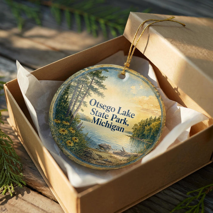 A round ornament in a box, featuring a scenic landscape of Otsego Lake, State Park, and Michigan.