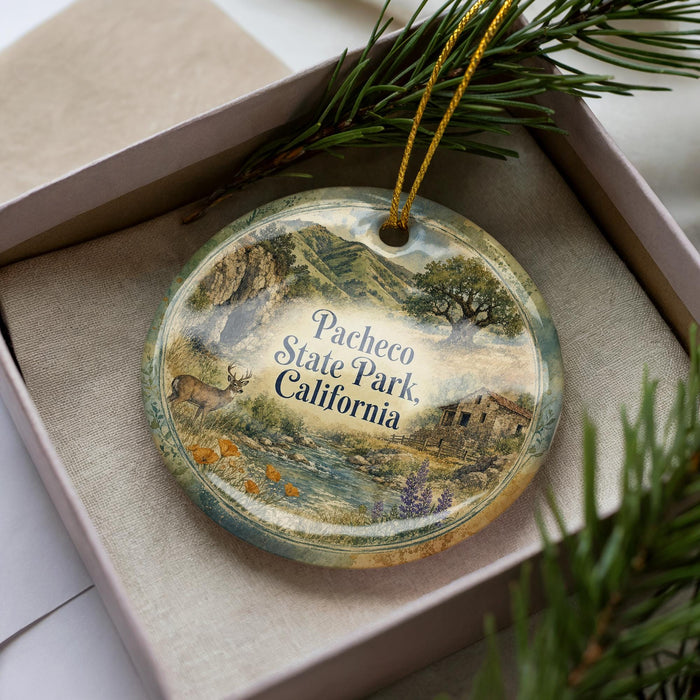 A decorative ornament with a landscape scene featuring a river, mountains, and a building, placed inside a box with pine branches.