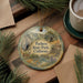 A decorative ornament with a scenic landscape of Pacheco State Park, California, featuring a deer, a river, and mountains. The ornament is hanging from a string and is placed on a wooden surface, surrounded by pine branches and a cup of coffee.
