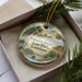 A decorative ornament in a box, featuring palm trees, a bird, and a body of water, with the text "Palmetto Island State Park, Louisiana" printed on it.