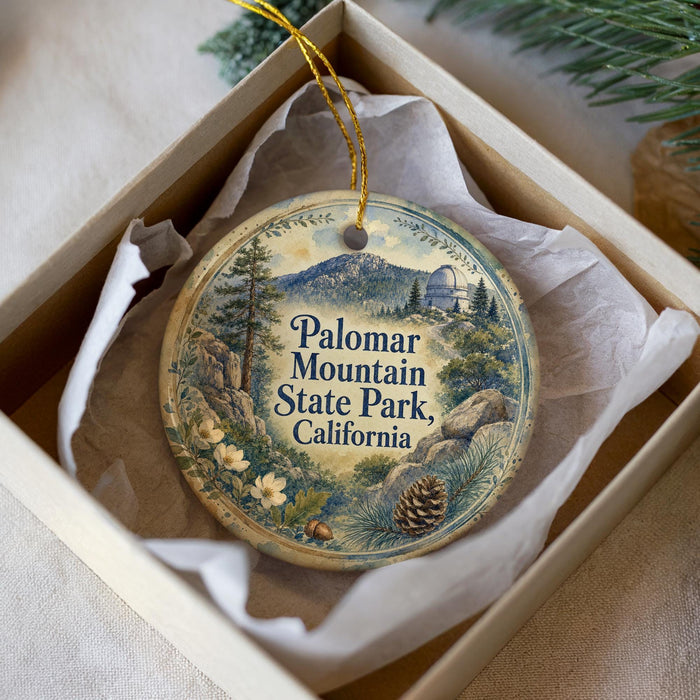 A decorative ornament in a white box, featuring a scenic landscape with mountains, pine trees, and flowers, along with the text "Palomar Mountain State Park, California".