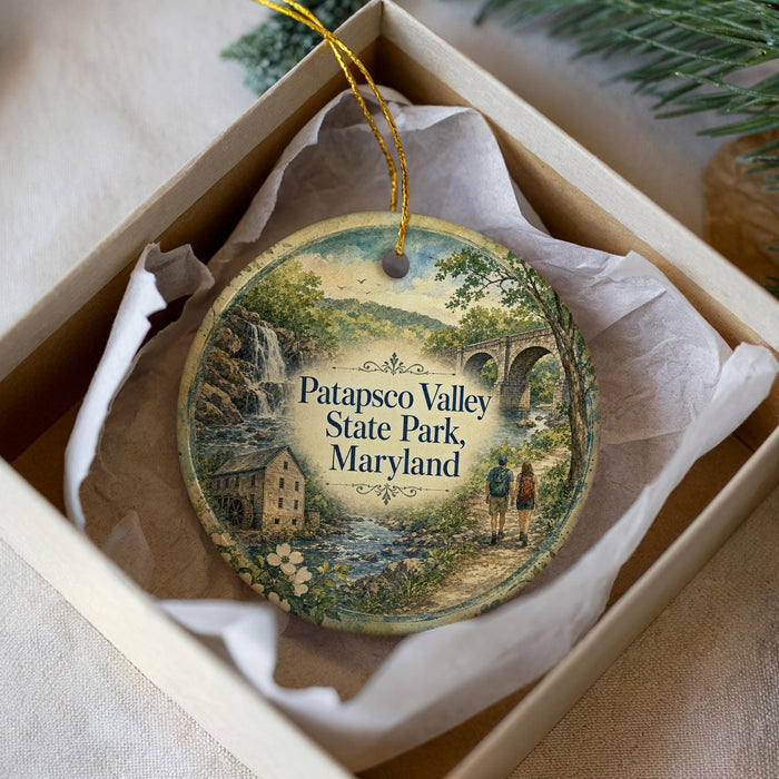 A decorative ornament in a box, featuring a scenic landscape with a waterfall, a bridge, and people walking along a path.