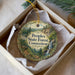 A decorative ornament in a box, featuring a scenic landscape with a waterfall, pine trees, and mountains.