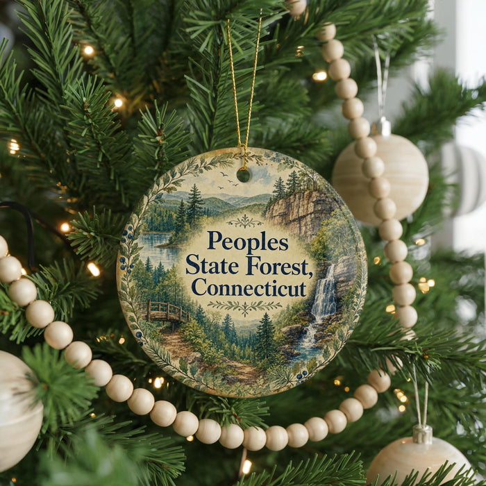 A Christmas tree decorated with ornaments, including a circular ornament with a scenic landscape and text that reads "Peoples State Forest, Connecticut".