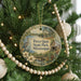 A round ornament hanging on a Christmas tree, featuring a scenic image of a park with a lake, trees, and a bird.
