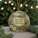 A round ornament with a painting of a park scene, featuring a bird, flowers, and a cabin, hanging from a string.