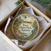 A decorative ornament in a box, featuring a scenic landscape with a building, trees, and a body of water.