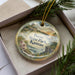 A decorative ornament with a scenic landscape of Perry State Park, Kansas, featuring a house, trees, and a body of water.