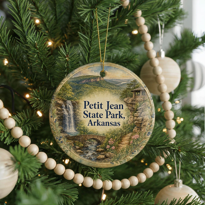A round ornament hanging on a Christmas tree, featuring a scenic landscape with a waterfall and a bridge.