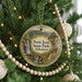 A round ornament hanging on a Christmas tree, featuring a scenic landscape with a waterfall and a bridge.