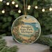 A round ornament with a scenic landscape of Petoskey State Park, Michigan, featuring a boat on the water, surrounded by pine trees and a cliff.