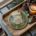 A decorative ornament with a scenic landscape of Big Sur State Park, California, featuring pine cones, a candle, and greenery.