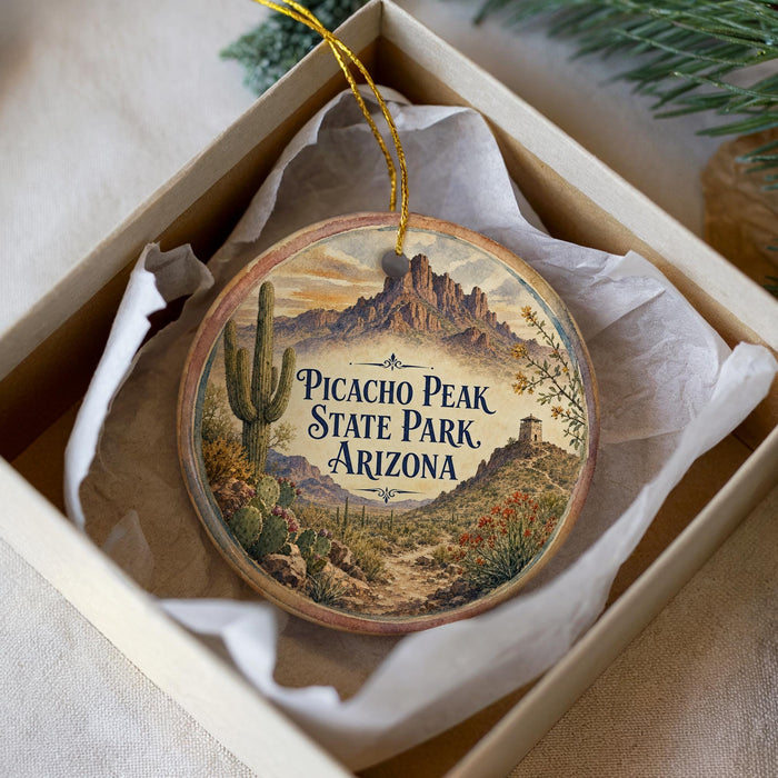 A decorative ornament in a box, featuring a desert landscape with mountains and cacti, along with the text "Picacho Peak State Park Arizona".