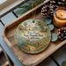 A decorative ornament featuring a scenic image of Pico Pico State Historic Park, California, with a candle and pine cones on a wooden tray.