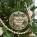 A round ornament hanging on a Christmas tree, featuring a scenic landscape with a waterfall, a cabin, and flowers.