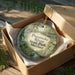 An oval ornament in a brown box, featuring a scenic image of the Potomac River and Maryland State Park.