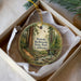 A round ornament with a painting of a forest scene, featuring a path leading through the trees and a stream running through the center.