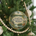 A round ornament hanging on a Christmas tree, featuring a scenic landscape with a lake and trees.