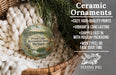 Ceramic ornaments, featuring a round ornament with a scenic landscape and text, are displayed in a basket with greenery.