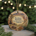 A round ornament with a desert landscape and mountains, featuring a wooden cabin and a tortoise, is displayed in front of a blurred background with Christmas lights.