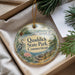 A decorative ornament with the text "Quaddick State Park, Connecticut" and an illustration of a bird, pine tree, and water, placed in a box with pine branches.