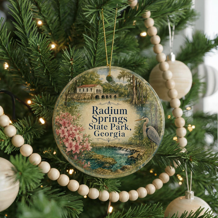 A round ornament hanging on a Christmas tree, featuring a scenic image of Radium Springs State Park in Georgia.