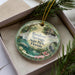 A decorative ornament in a box, featuring a scenic image of Rainbow Springs State Park in Florida.