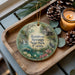 A decorative ornament featuring a scenic image of Rainbow Springs State Park in Florida, with pine cones and a lit candle on a wooden tray.