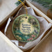 A decorative ornament in a white box, featuring a scenic illustration of a park with a waterfall, a bird, and flowers.