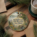 A decorative ornament with a scenic landscape, featuring a lake, bridge, and mountains, hangs on a wooden surface.