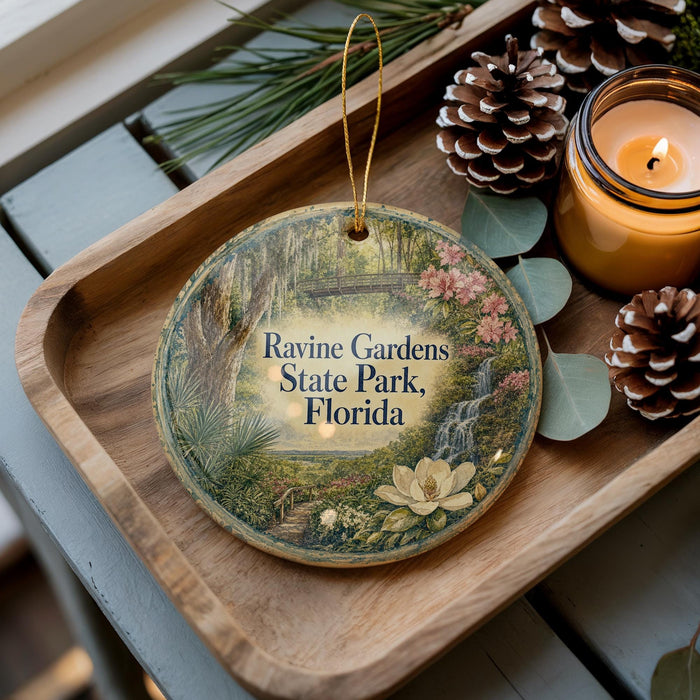 A wooden tray with a decorative ornament featuring a scenic image of the Raine Gardens State Park in Florida, accompanied by pine cones and a lit candle.
