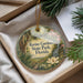 An ornament with a floral design hangs from a string, placed inside a box with pine branches and a white card.