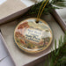 A decorative ornament with a scenic image of the Red Rock Canyon State Park in California, featuring a mountain landscape and a tree.