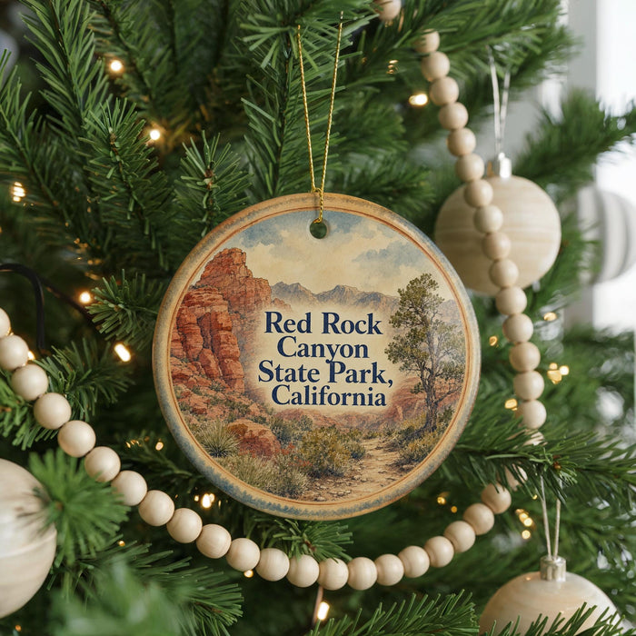 A round ornament hanging on a Christmas tree, featuring a scenic image of the Red Rock Canyon State Park in California.