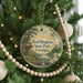 A round ornament hanging on a Christmas tree, featuring a scenic landscape with a waterfall and a cabin.