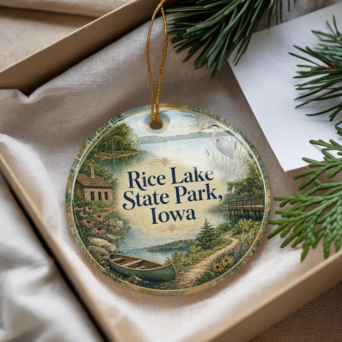 A decorative ornament with a scenic landscape of Rice Lake State Park, Iowa, featuring a boat, a house, and a bird.