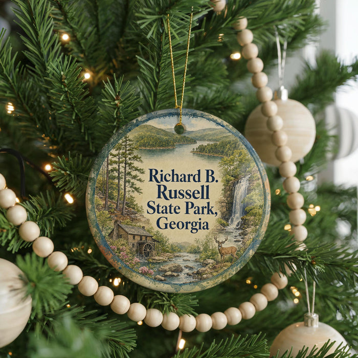 A round ornament hanging on a Christmas tree, featuring a scenic image of a lake and mountains with a waterfall.