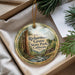 A round ornament with a scenic image of a forest and a stream, hanging from a string.