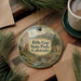 A decorative ornament featuring a scenic landscape with mountains, a river, and pine trees, hanging on a wooden surface.