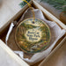 A decorative ornament in a box, featuring a scenic landscape with a river, trees, and a bridge.