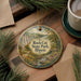 A decorative ornament featuring a scenic landscape of Rock Cut State Park in Illinois, with a stream and trees, is displayed on a wooden surface alongside a cup of coffee and some pine branches.