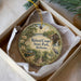 A round ornament with a scenic landscape of Roland Cooper State Park, Alabama, displayed in a box with a white tissue paper lining.