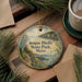 A circular ornament with a scenic landscape of Roque Bluffs State Park, Maine, hangs on a wooden surface.