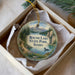 A round ornament in a box, featuring a scenic landscape with mountains, a lake, and a bird, along with the text "Round Lake State Park, Idaho".