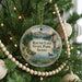 A round ornament hanging on a Christmas tree, featuring a scenic landscape with mountains, a lake, and a bird in the water.