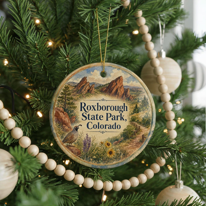 A round ornament hanging on a Christmas tree, featuring a scenic image of the Rocky Mountains and the words "Roxborough State Park, Colorado".